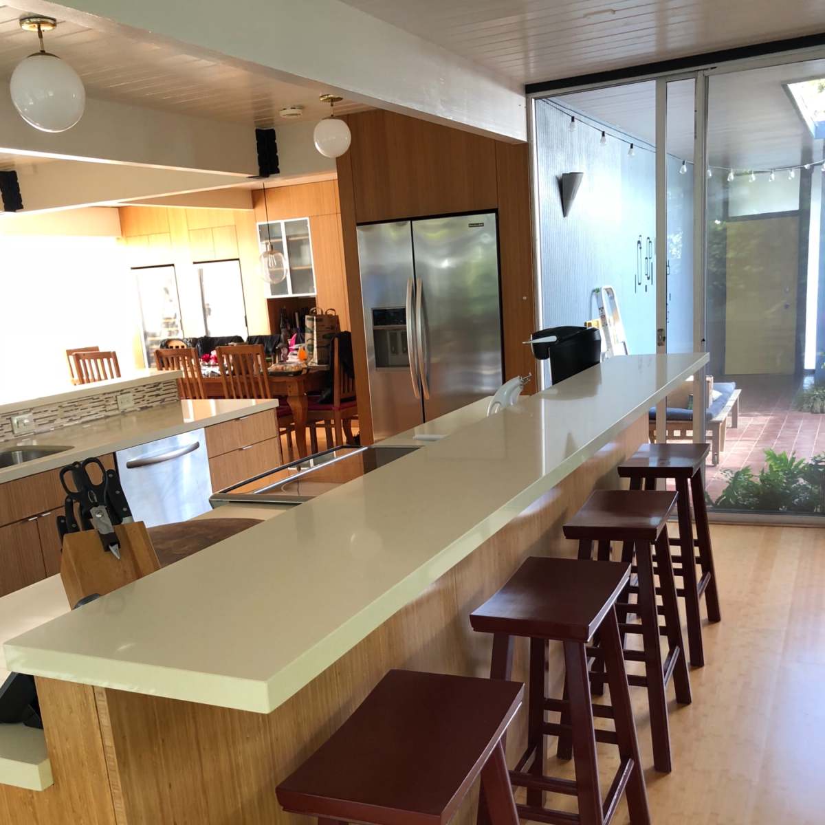 A modern kitchen with a long, white countertop and four maroon stools positioned along one side.