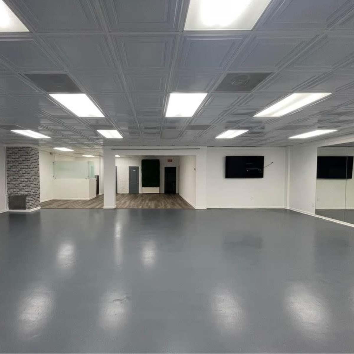 A spacious, well-lit room with a smooth gray floor and a mirrored wall, featuring a reception area in the background.