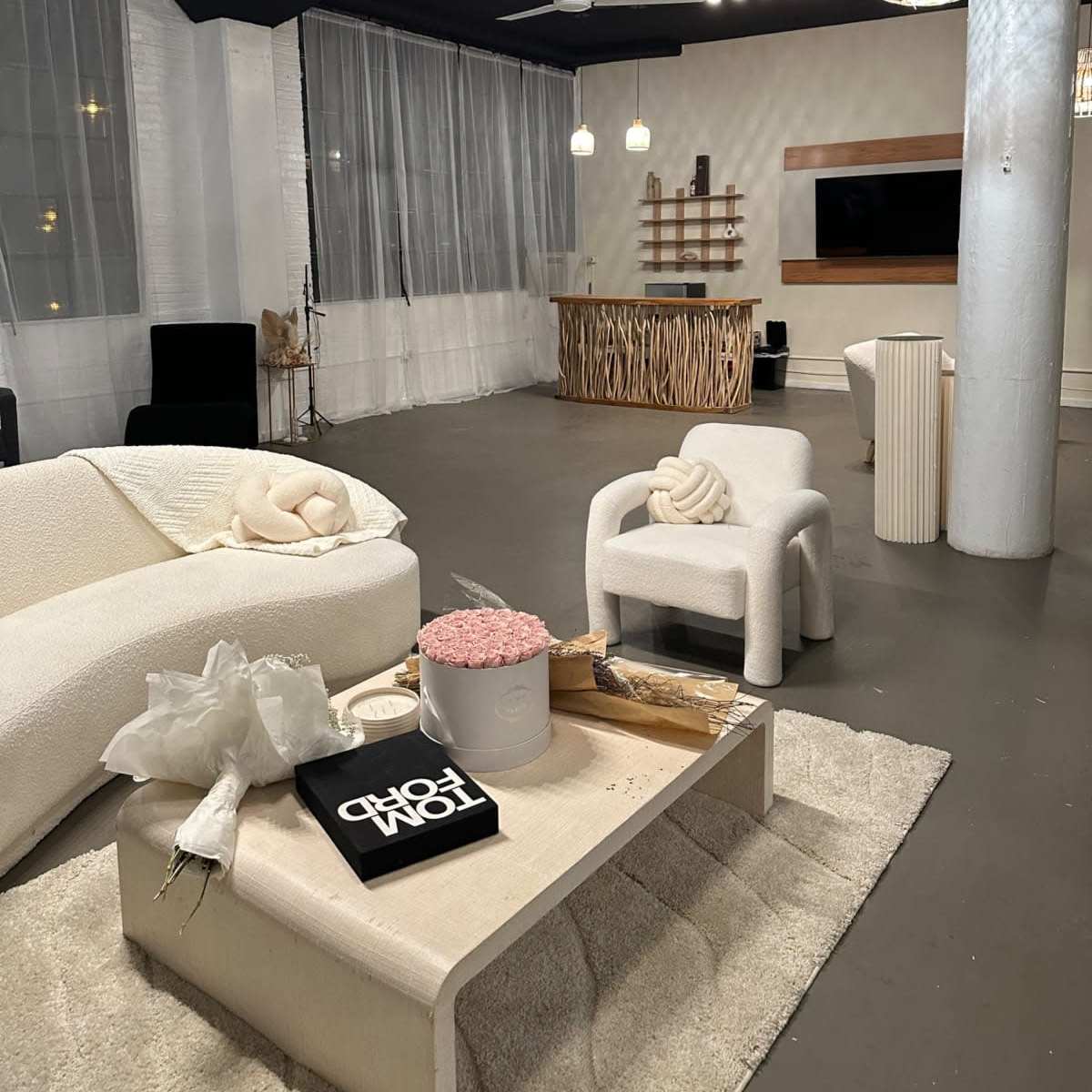 A modern, minimalist living space featuring a light-colored sofa, decorative elements on a coffee table, and a wooden feature wall with a television.