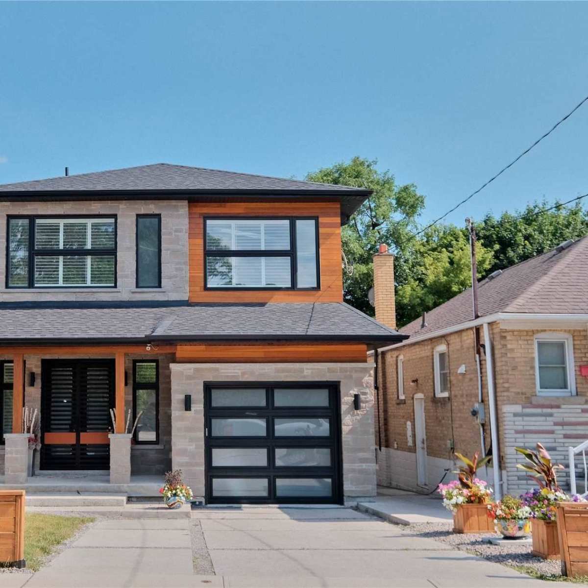 A modern two-story house with a mix of stone and wood siding, a black garage door, and landscaped front yard.