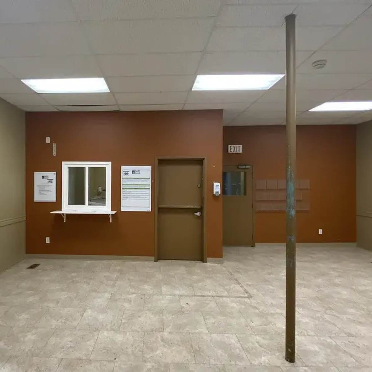 A vacant room with beige tile flooring, painted walls in two colors, and a door and window on one side.