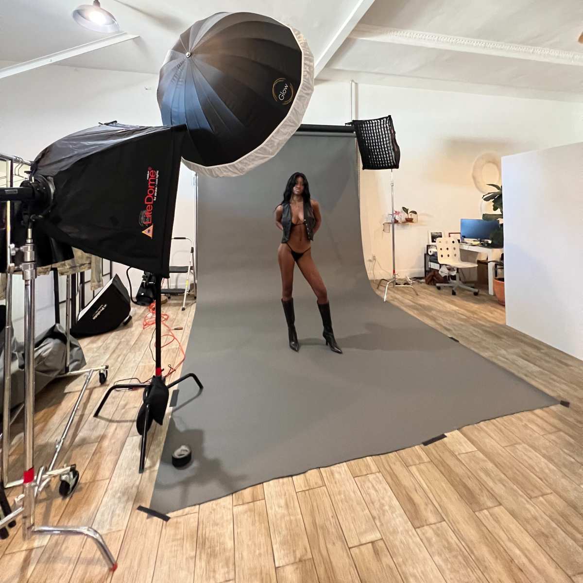 A model poses in a photography studio equipped with lighting and backdrop setups.
