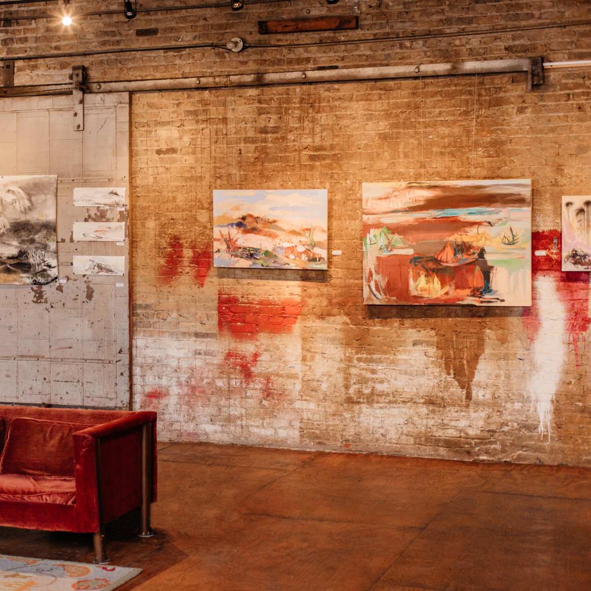 A modern art gallery featuring a red velvet sofa against a brick wall adorned with abstract paintings.