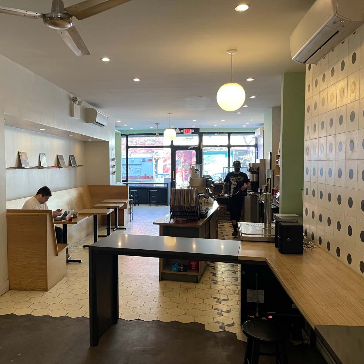 A spacious café interior with seating areas, a counter, and large front windows that allow natural light in.