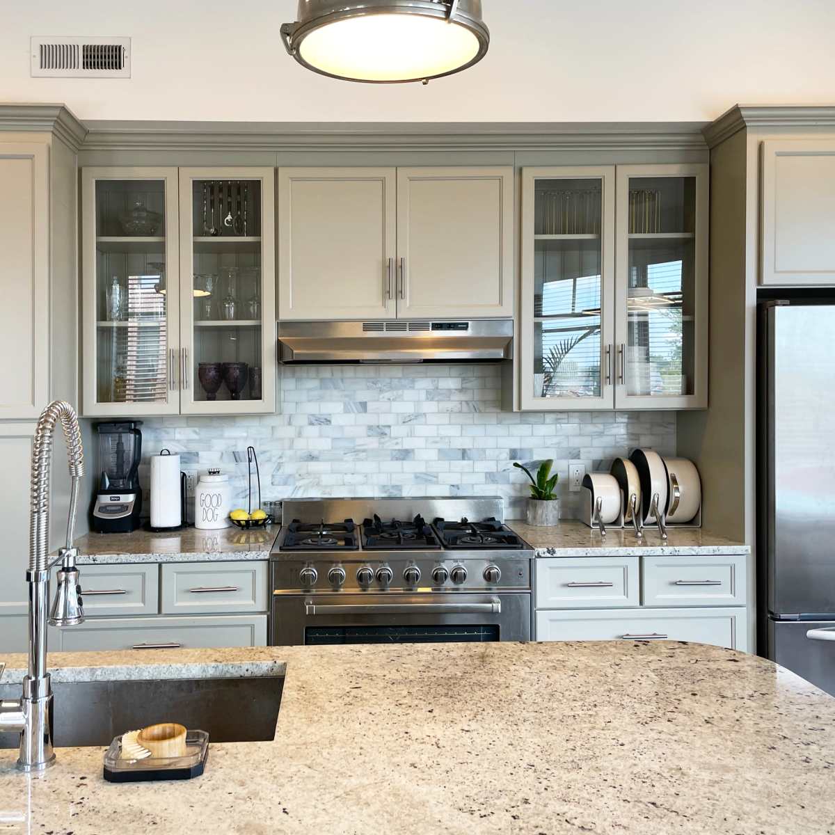 A modern kitchen features light cabinetry, a marble backsplash, stainless steel appliances, and a large island with a sink.