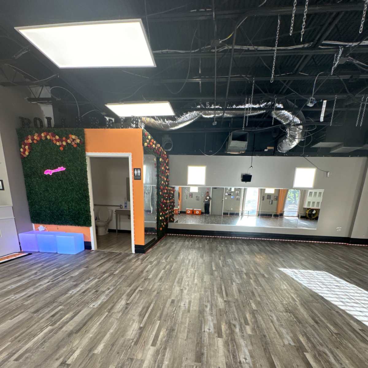 A spacious studio with wooden flooring, a mirrored wall, and decorative elements, including greenery and orange accents.