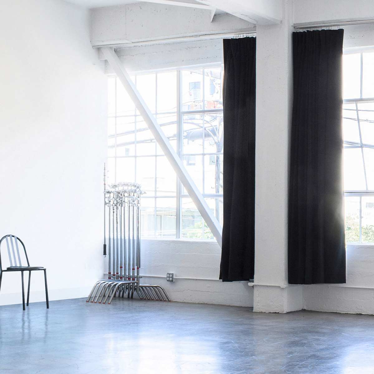 A spacious, minimalist room with large windows, a black chair, and a studio light on a stand.