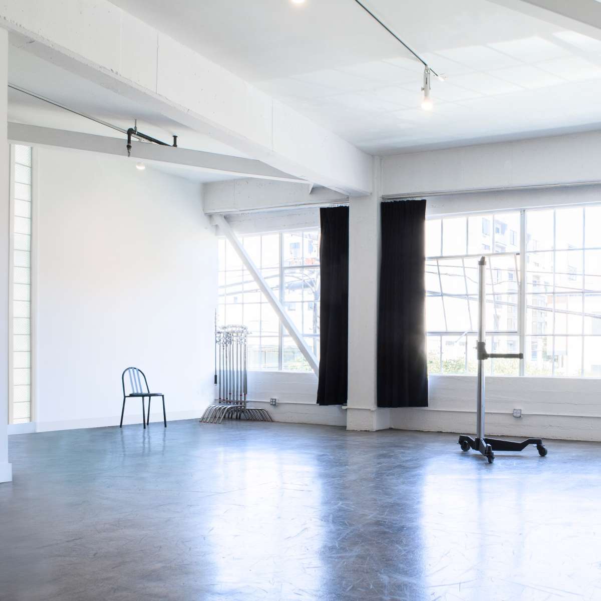 A spacious, well-lit studio with large windows, two black chairs, and a minimalistic design.