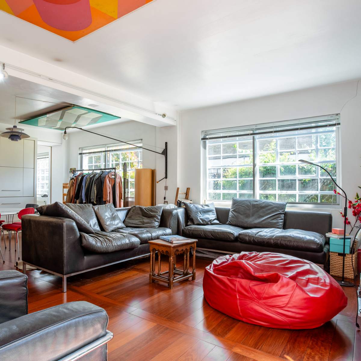 A modern living room equipped with a large leather sectional sofa, a red bean bag, and a dining area featuring circular red chairs.