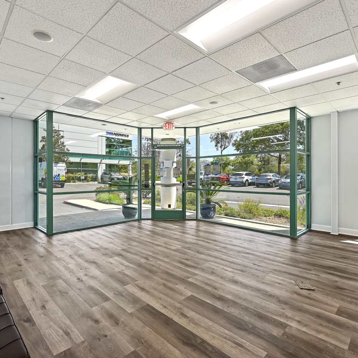 A modern office lobby with large glass windows, wooden flooring, and a seating area.