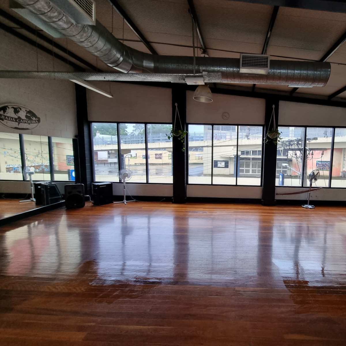An empty dance studio with wooden floors and large windows overlooking an outdoor landscape.