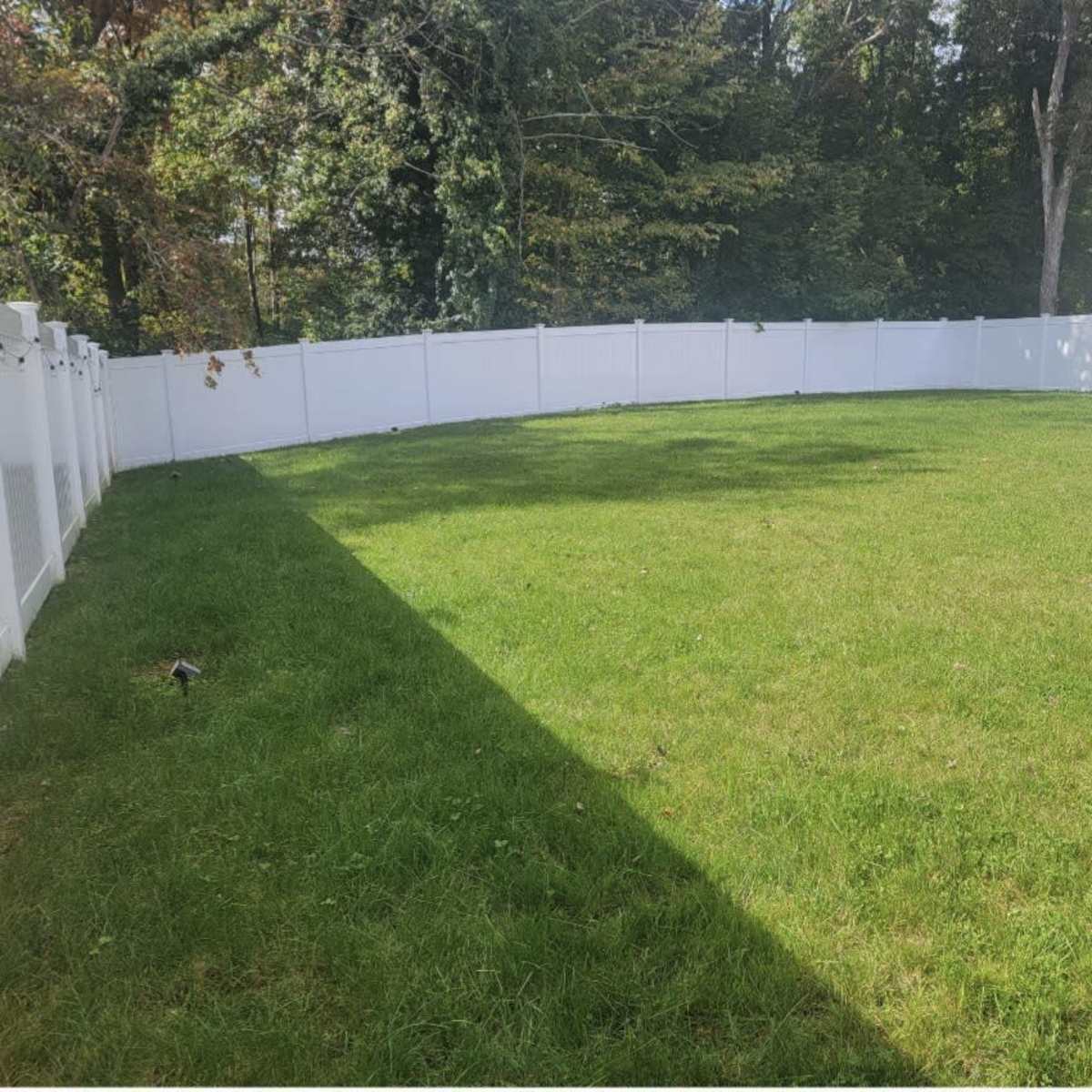 A large, flat grassy area enclosed by a white fencing in a backyard.
