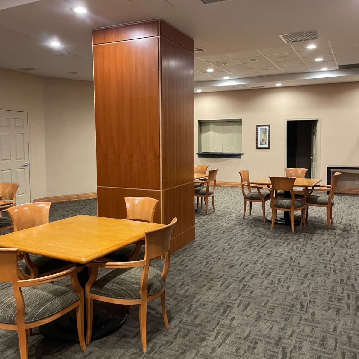 A spacious room with wooden dining tables and chairs arranged around a central wooden pillar.