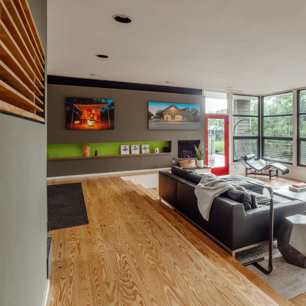 A modern living room with large windows, a dark sofa, a coffee table, and decorative art on the walls.