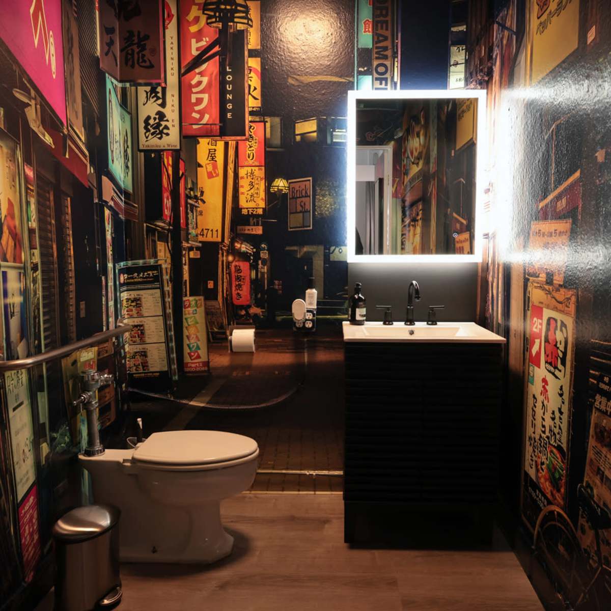 A modern bathroom features a wall adorned with vibrant urban-themed wallpaper, a sleek sink cabinet, a toilet, and a backlit mirror.