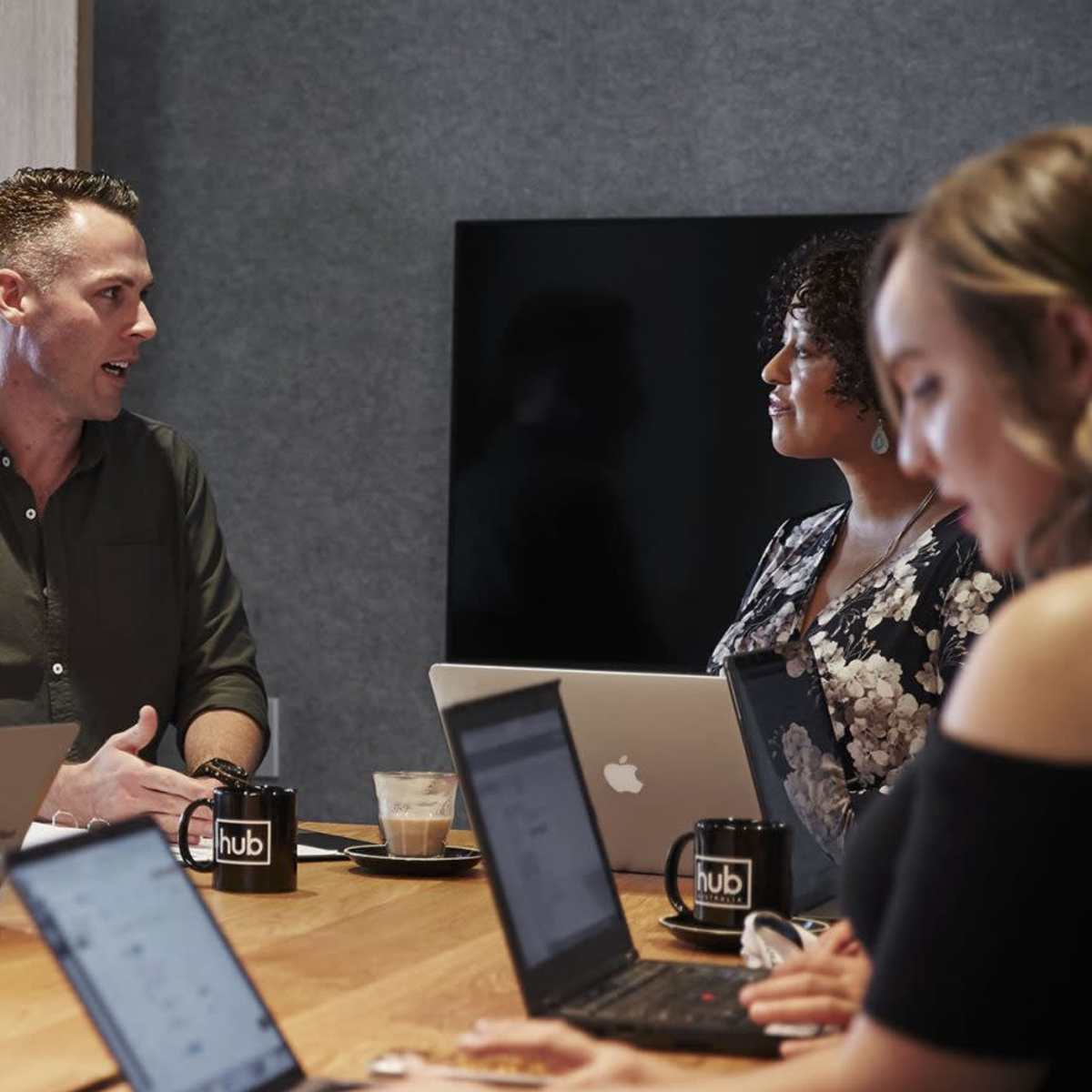 A group of professionals sit around a conference table, engaged in discussion with laptops open in front of them.