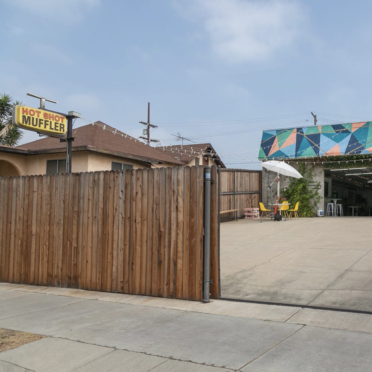 A fenced area with a concrete surface leads to a colorful building, marked by a sign for "Hot Shot Muffler" overhead.