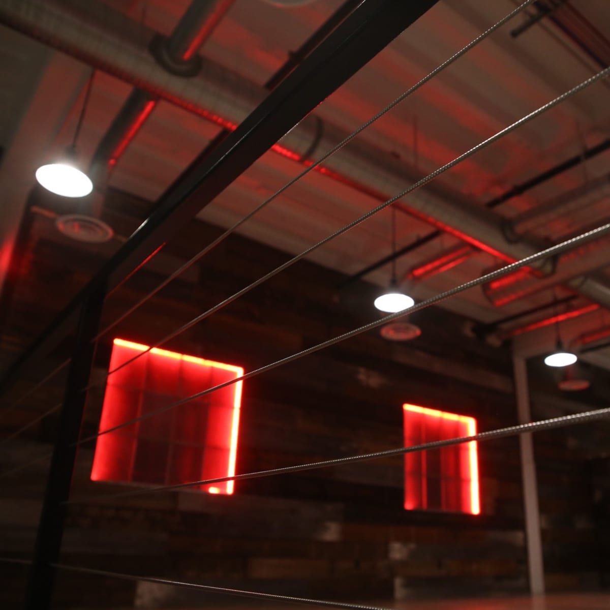 An interior space with industrial elements, featuring red-lit windows and metal cable railings.