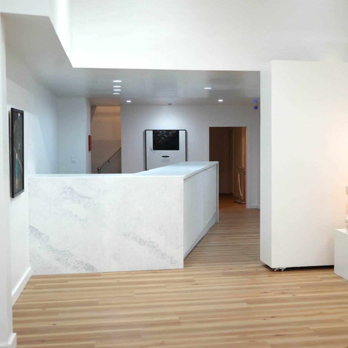 A modern, minimalist interior with a white reception desk, light wood flooring, and illuminated sculptural lamps in the corner.