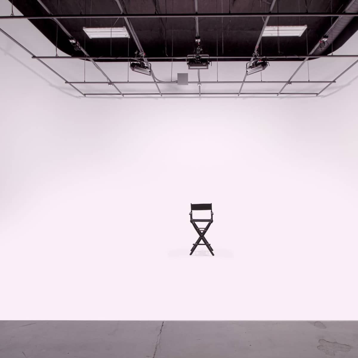 A single black director's chair is positioned in the center of a spacious, empty white studio.
