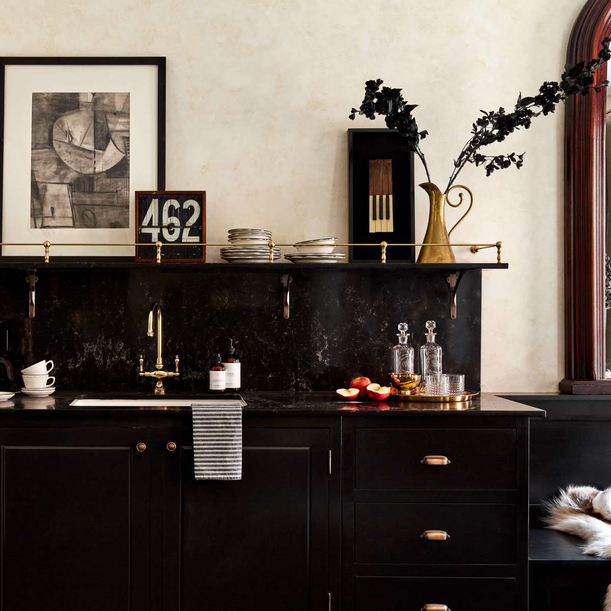 A black kitchen counter with a coffee maker, decorative items, and a wall shelf displaying books and a framed artwork.