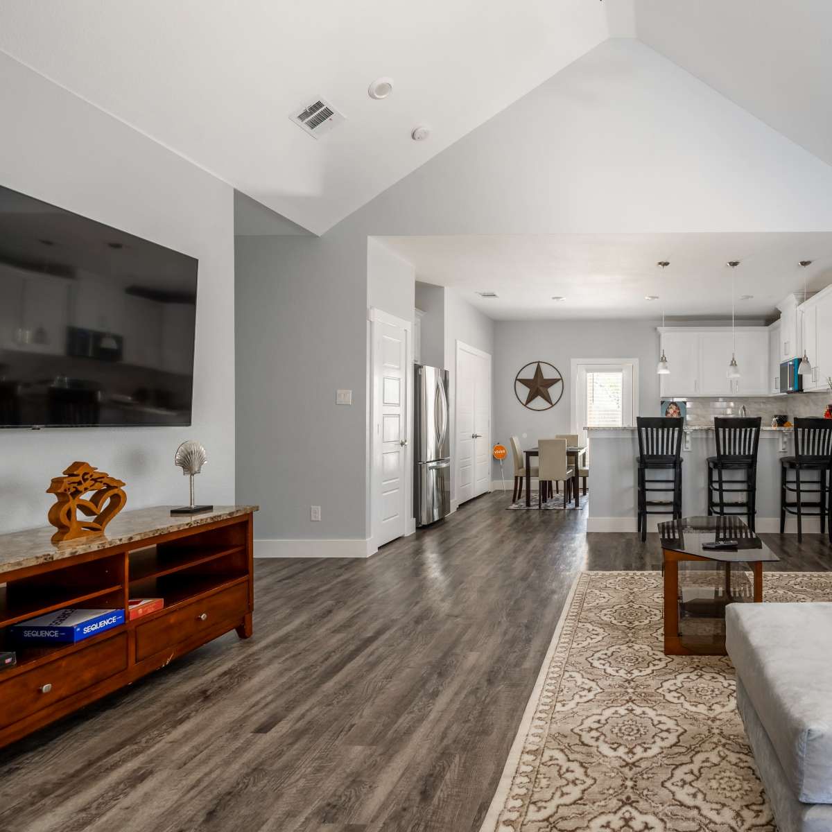 A living room with a sectional sofa, a wooden coffee table, a flat-screen TV, and an adjacent kitchen with bar seating.