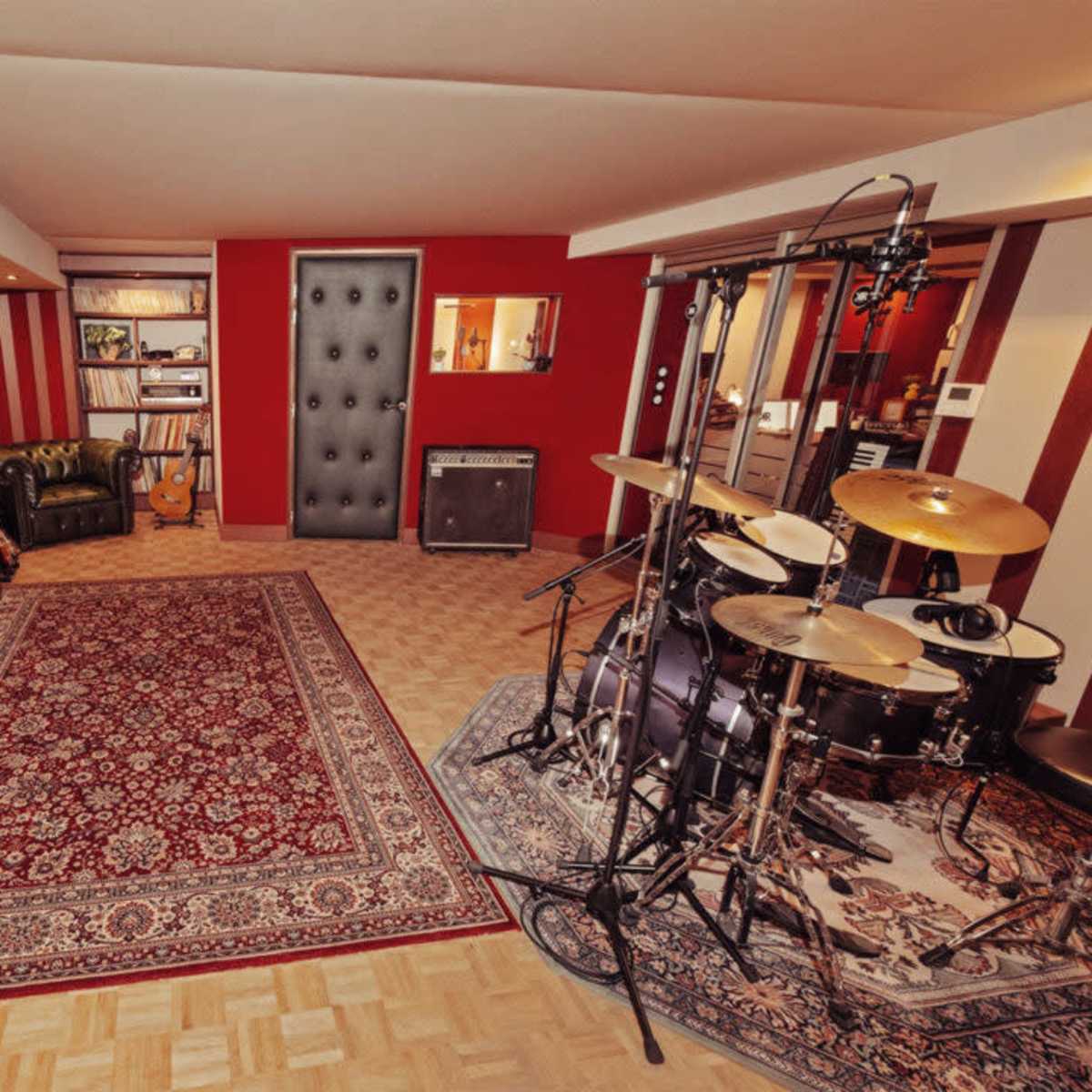 A well-equipped music studio featuring a drum set, a keyboard, a guitar, and a decorative plant, all arranged on a patterned rug.