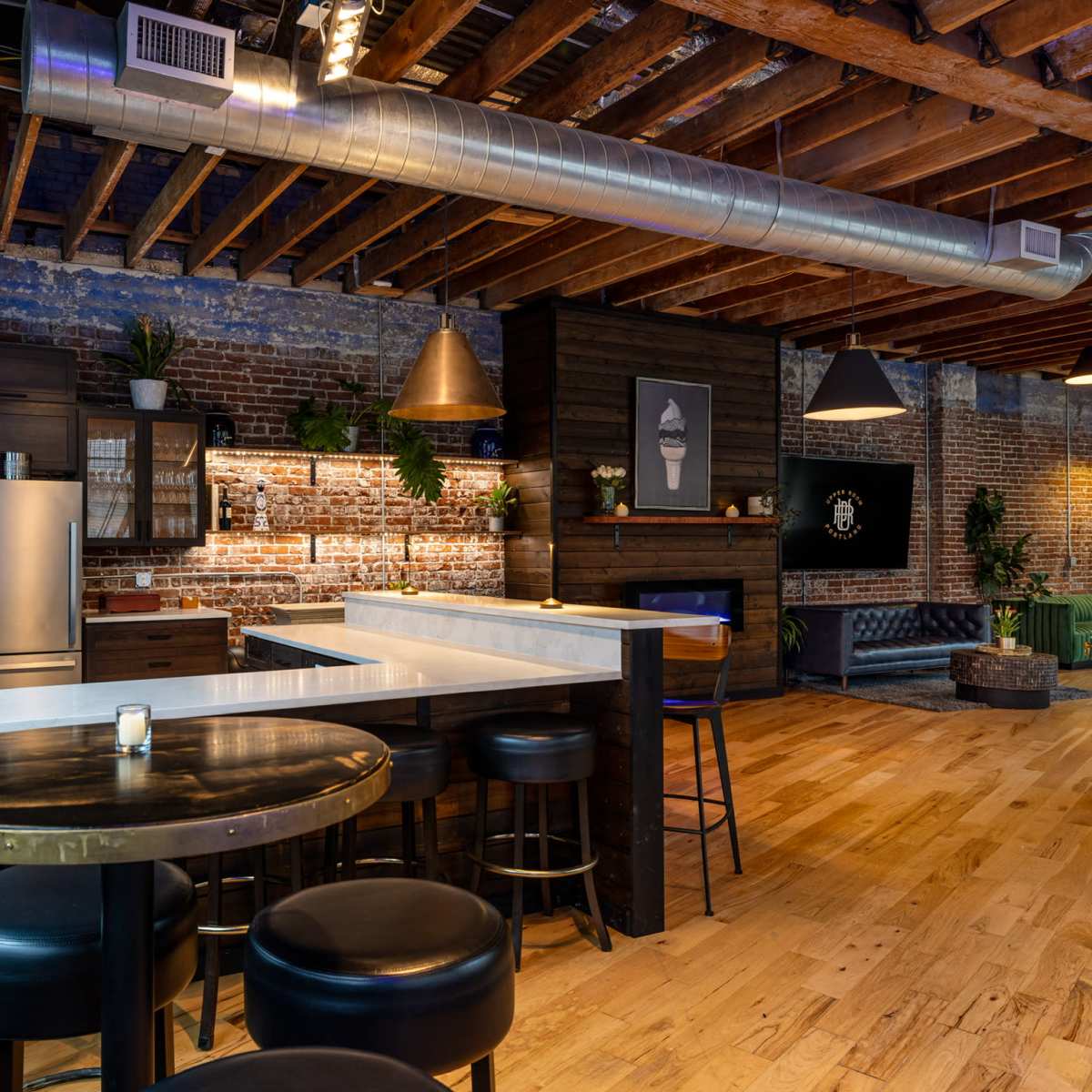 A modern kitchen and dining area featuring exposed brick walls, wooden beams, a central island with a white countertop, and various seating options.
