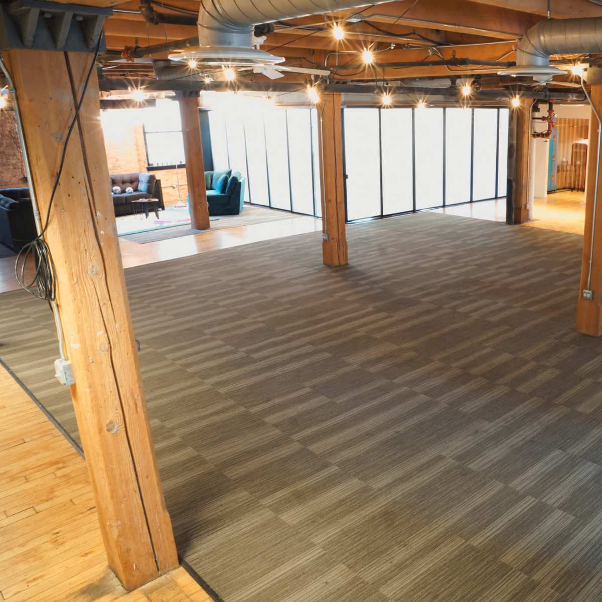 A spacious interior with wooden beams and a carpeted floor, featuring large windows that allow natural light to enter.