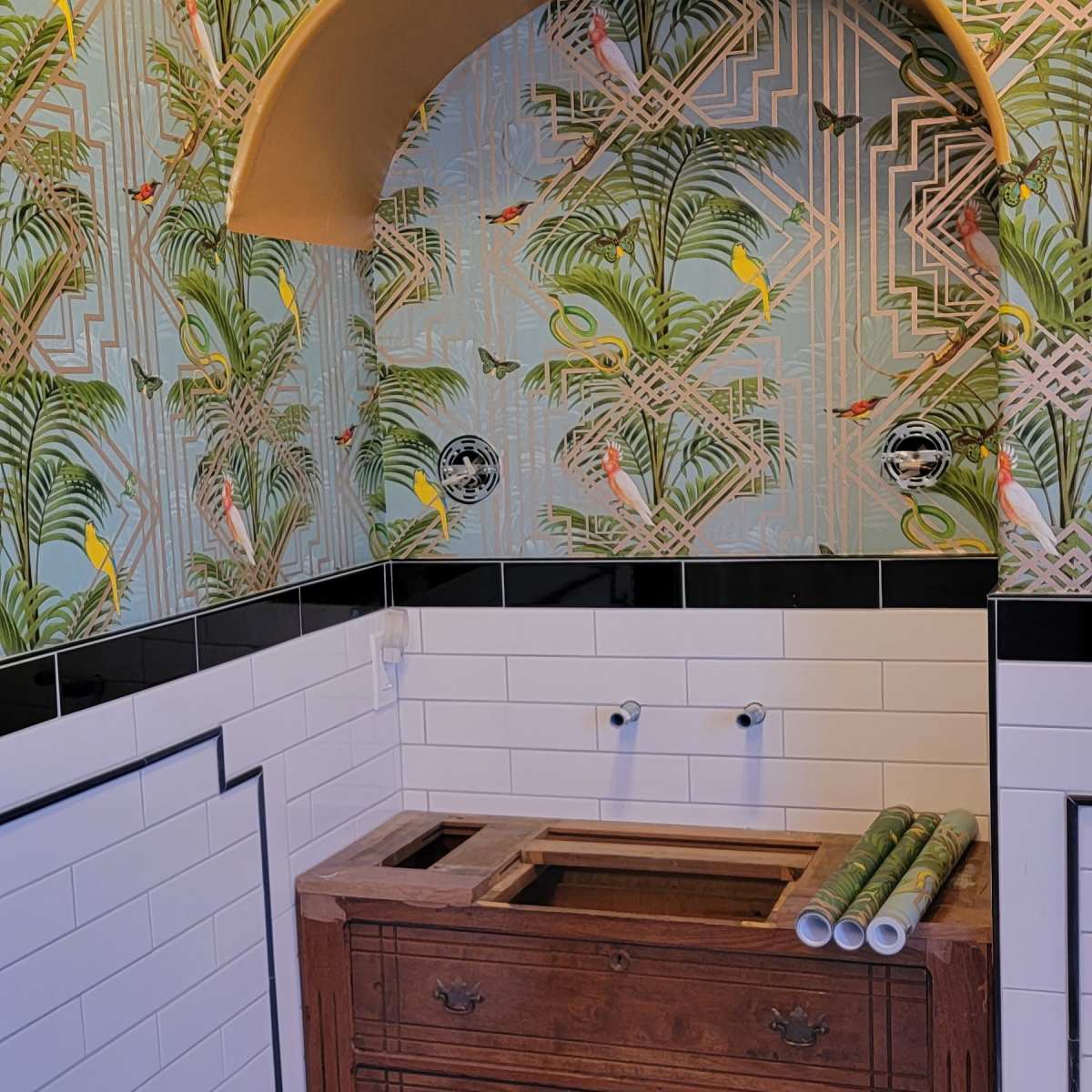 A bathroom with a vintage wooden dresser as a sink cabinet, decorated with tropical leaf-patterned wallpaper and geometric tile accents.