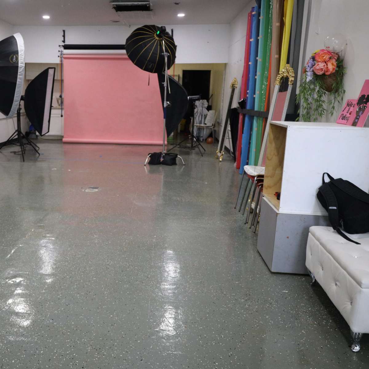 A photography studio with equipment, including softbox lights and a pink backdrop, set against a polished floor.