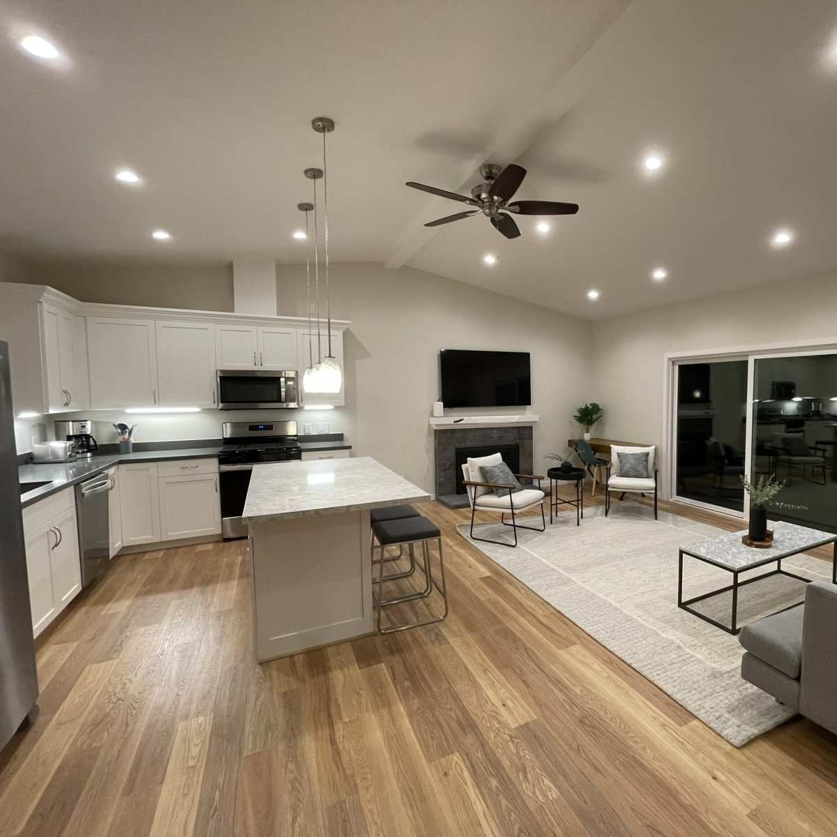 A modern open-concept living space with a kitchen, dining area, and seating area featuring contemporary furniture and a large window.