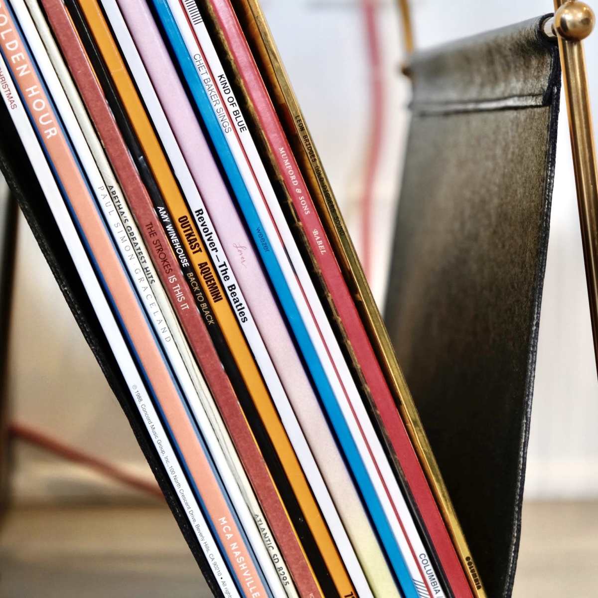 A collection of vinyl records is neatly arranged in a black holder with a brass frame.