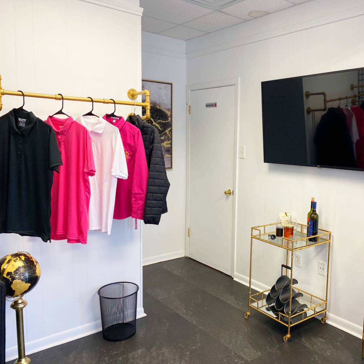 A neatly arranged room featuring a clothing rack with shirts, a wall-mounted television, a decorative cart with a bottle, and a globe stand.