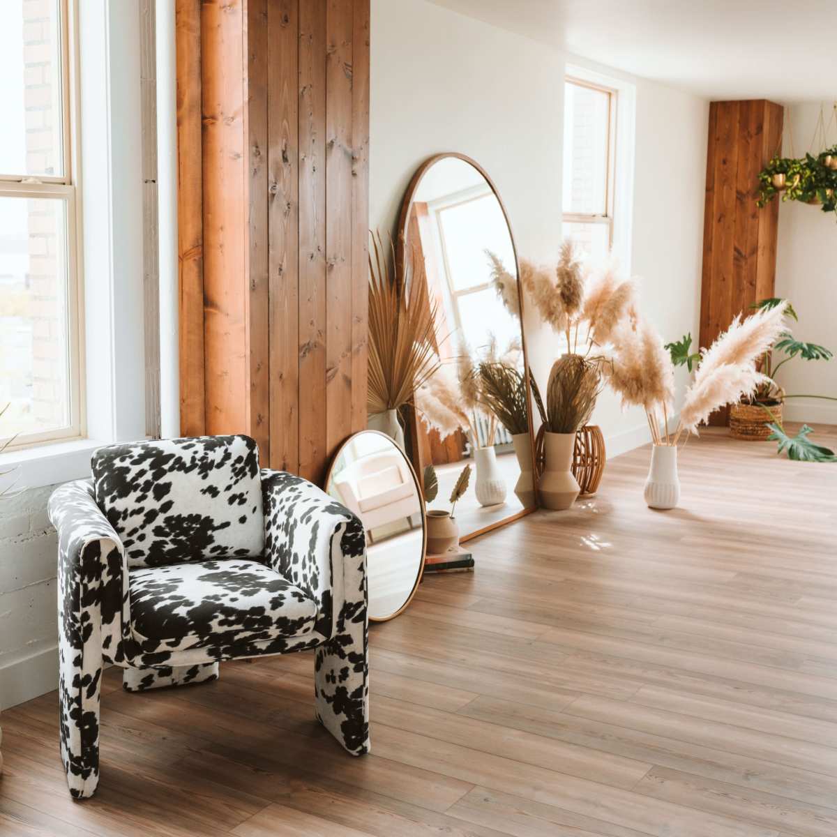 A spacious interior with a cow-print armchair, plants in decorative vases, and large windows allowing natural light to enter.
