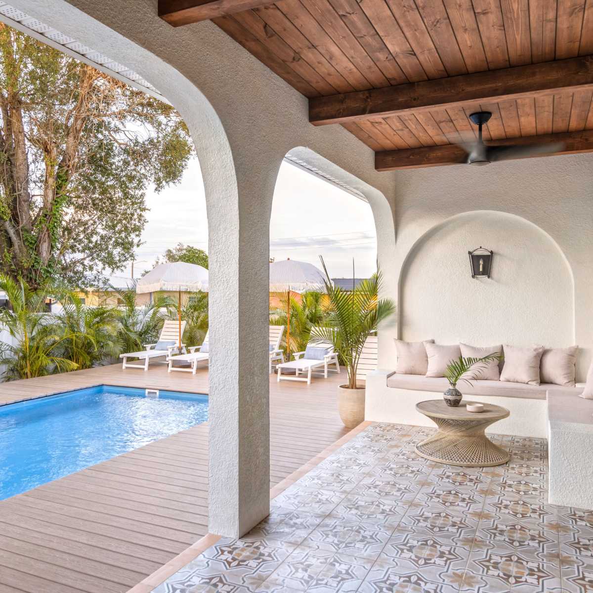 A patio area featuring a swimming pool, a wooden deck, and a seating arrangement under an overhanging porch.