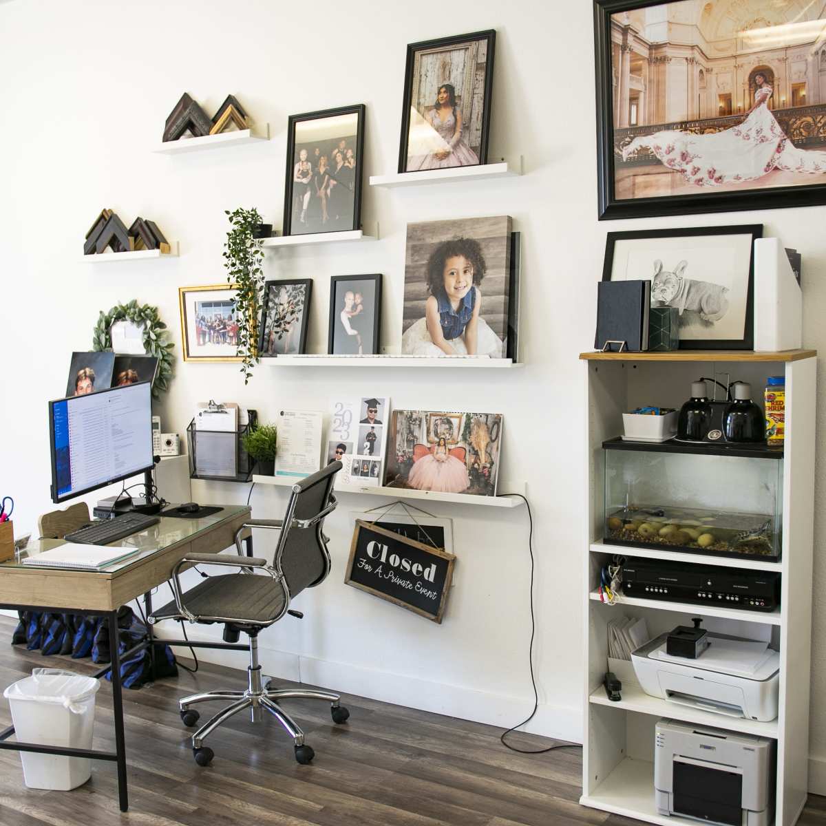 A modern office space with a desk, computer, and wall shelves displaying various framed photographs and decorative items.