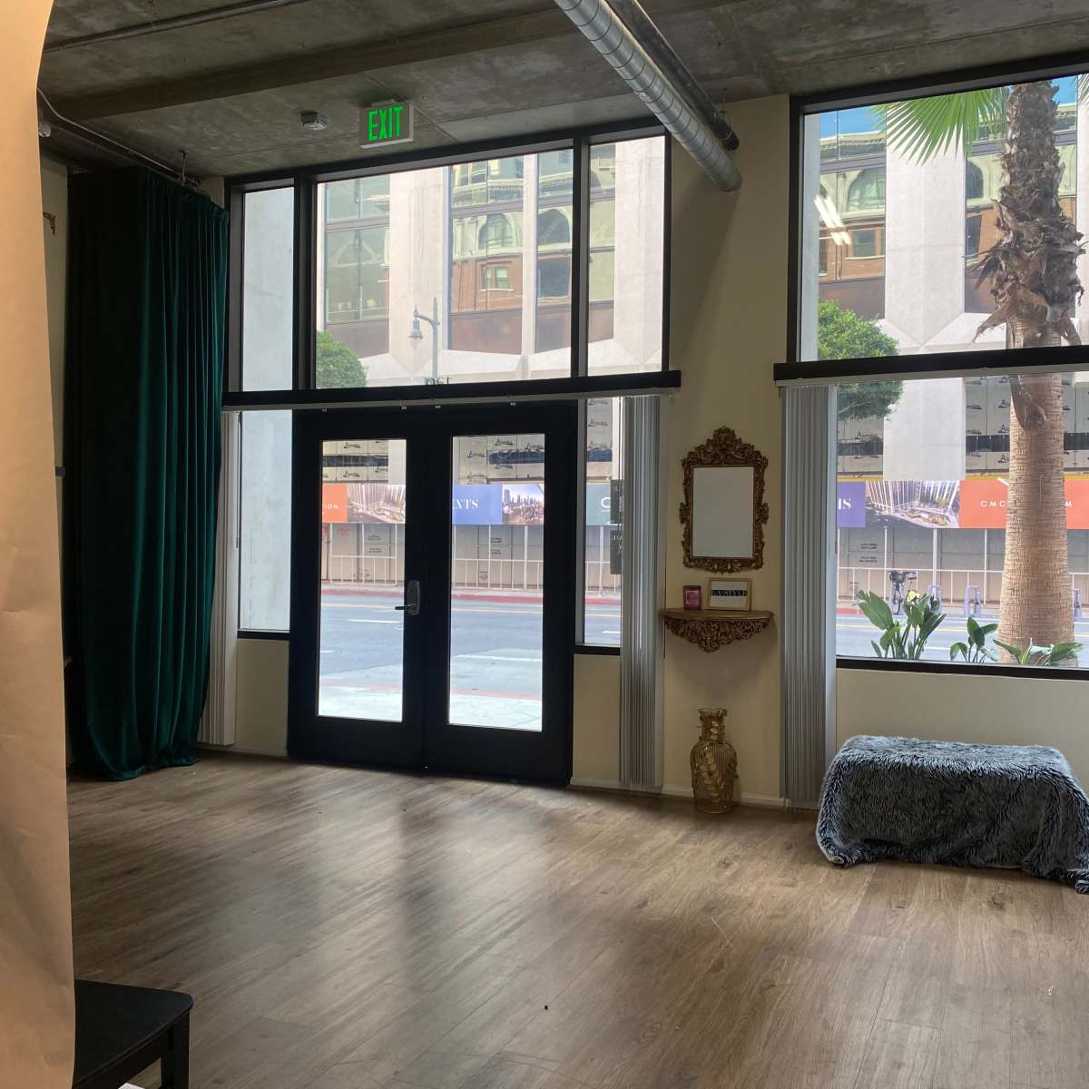 The scene shows an interior space with large windows, a bench covered with a blue cloth, a decorative mirror on the wall, and palm trees visible outside.