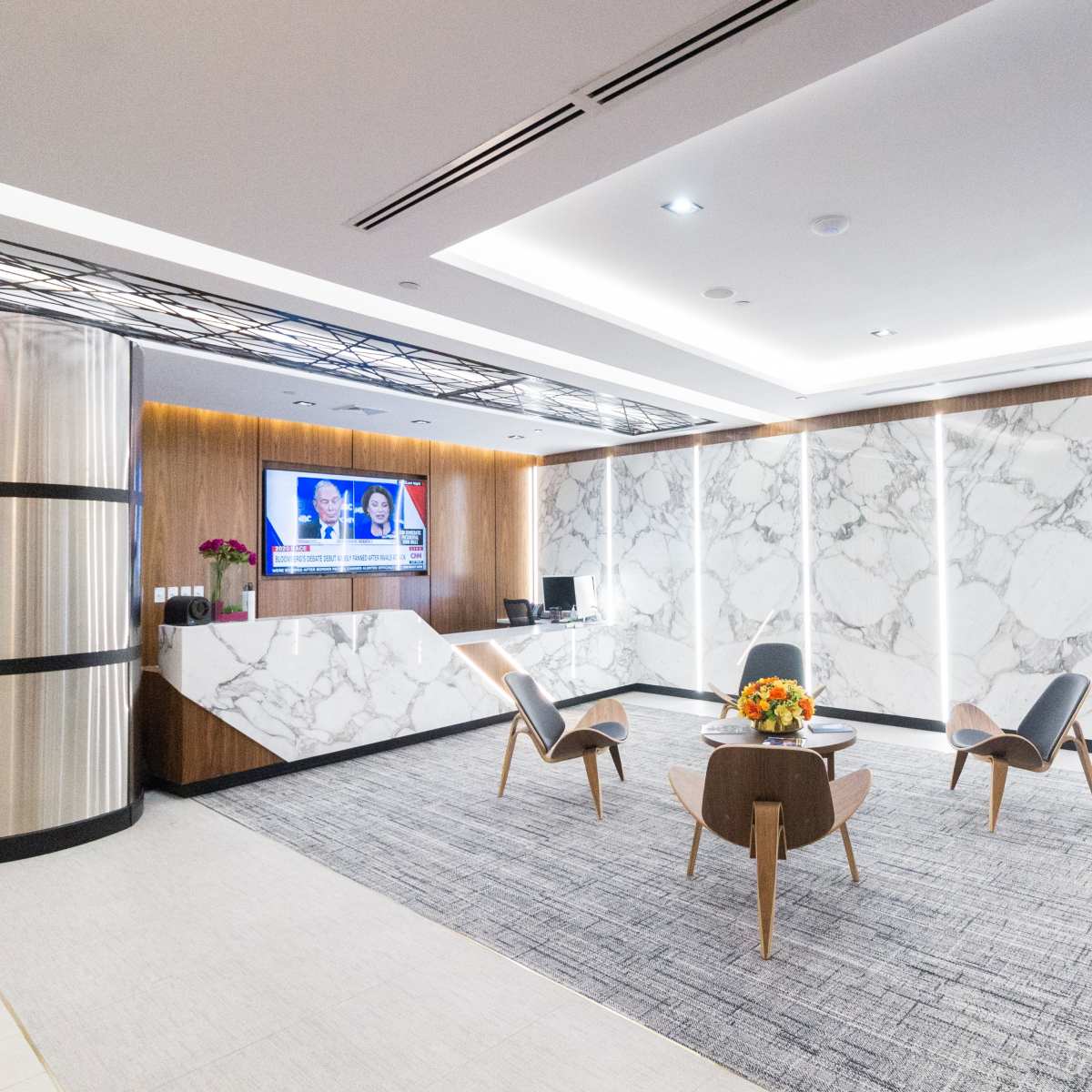 A modern reception area featuring marble walls, stylish seating, and a television displaying news.