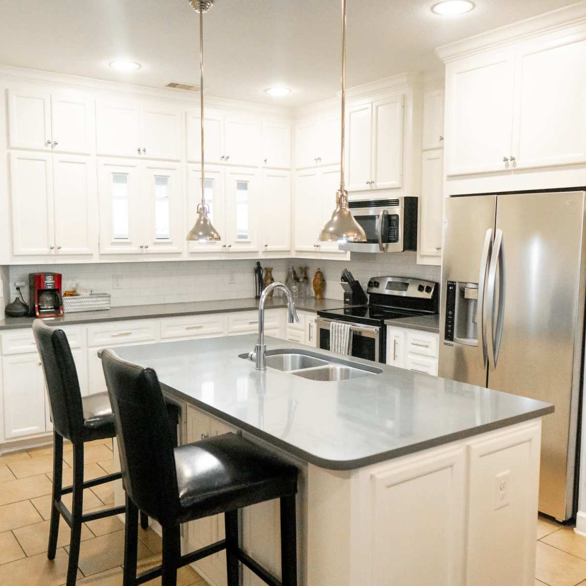 A modern kitchen with white cabinetry, stainless steel appliances, and an island with two black barstools.