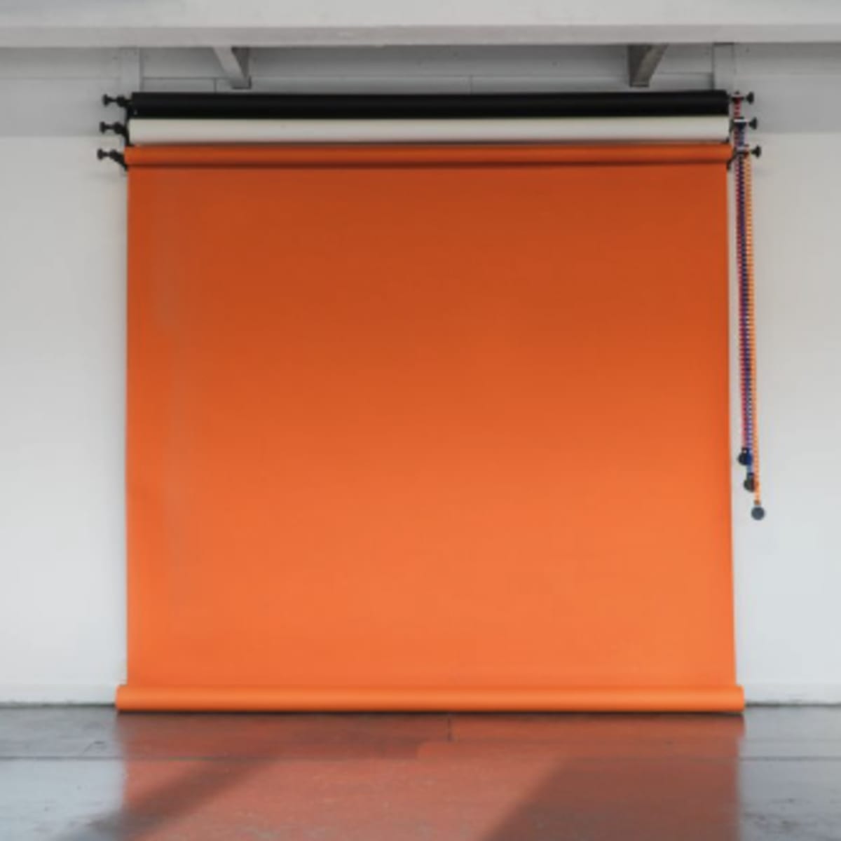 An empty room with a large orange backdrop roll hanging from a mounting system on the wall.