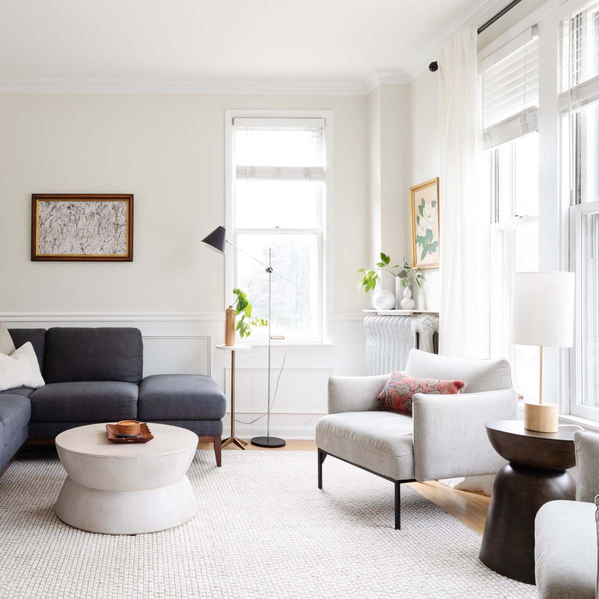 A modern living room with a gray sectional sofa, a round coffee table, and large windows allowing natural light to enter the space.
