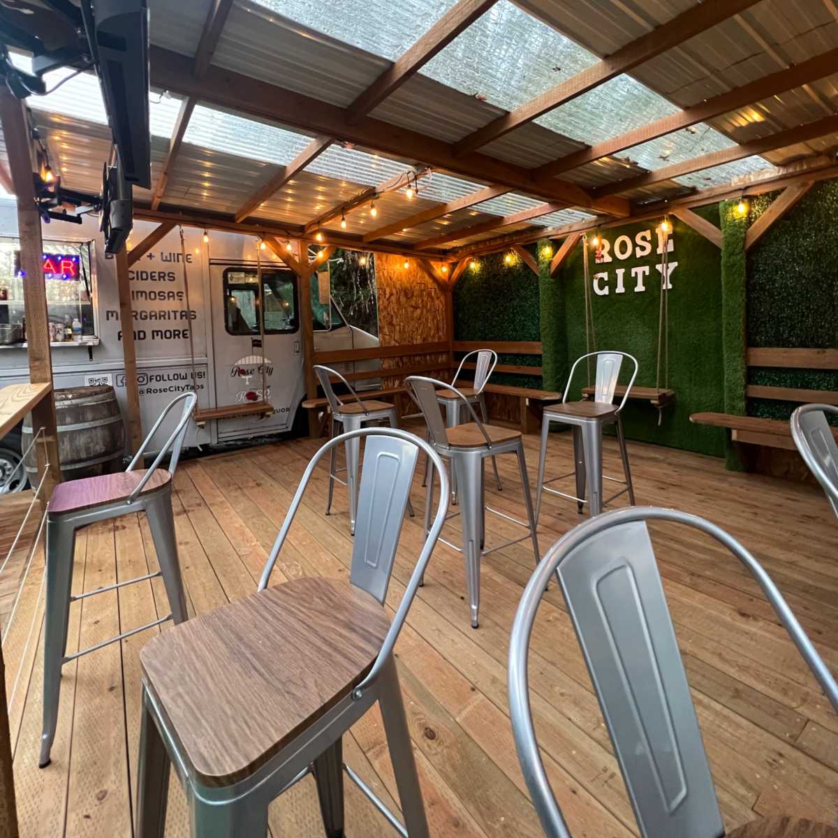 An outdoor seating area with metal chairs, wooden tables, and string lights under a covered roof.