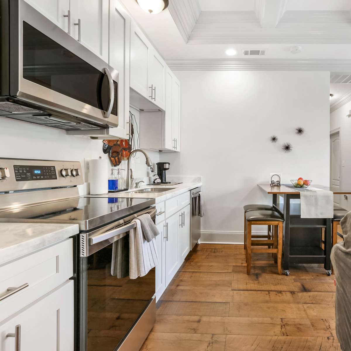A modern kitchen with stainless steel appliances, white cabinetry, and a small dining area with two barstools.