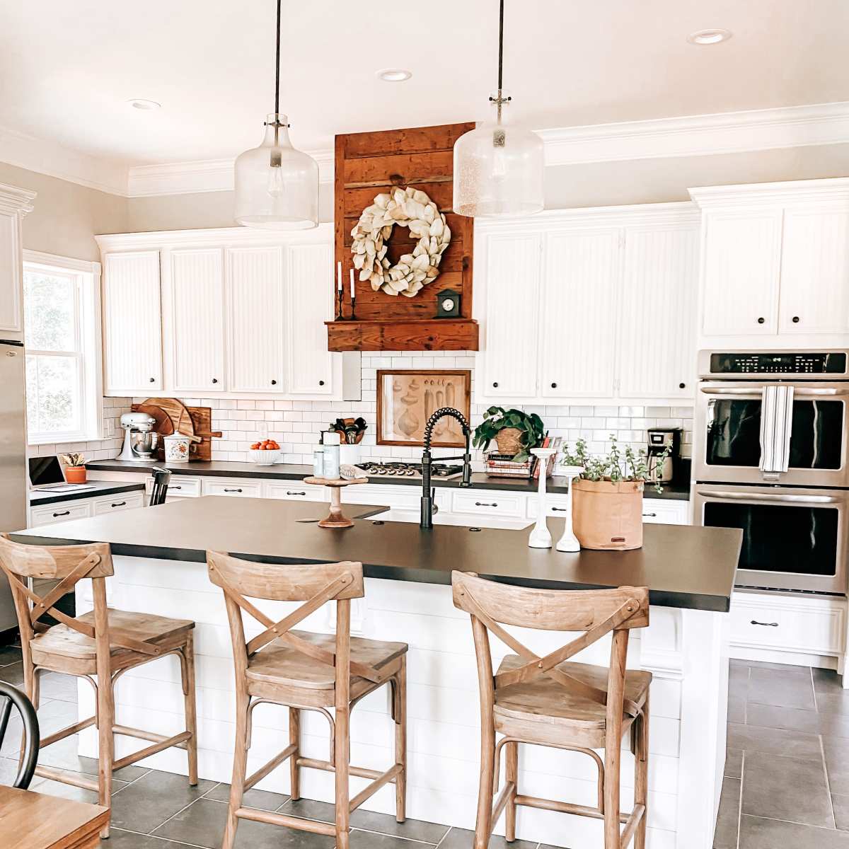 A modern kitchen features white cabinetry, a dark countertop, wooden bar stools, and pendant lighting over an island with decorative elements.