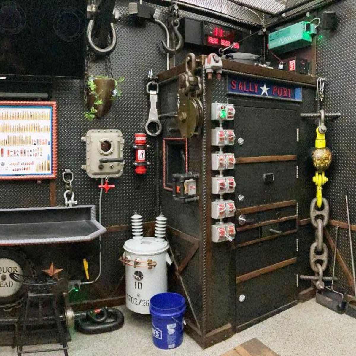 A wall filled with industrial tools and equipment, including chains, a large door, and various metallic objects, arranged in a dimly lit space.