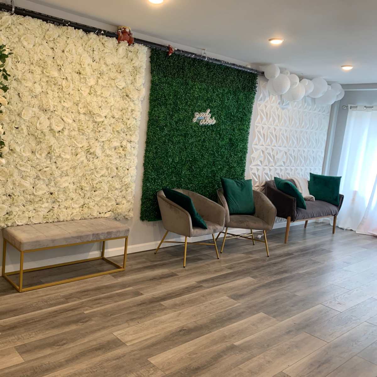 The scene features a modern interior space with a flower-covered wall on one side, a green wall of greenery on the other, and two gray chairs with green cushions arranged in front of a bench.