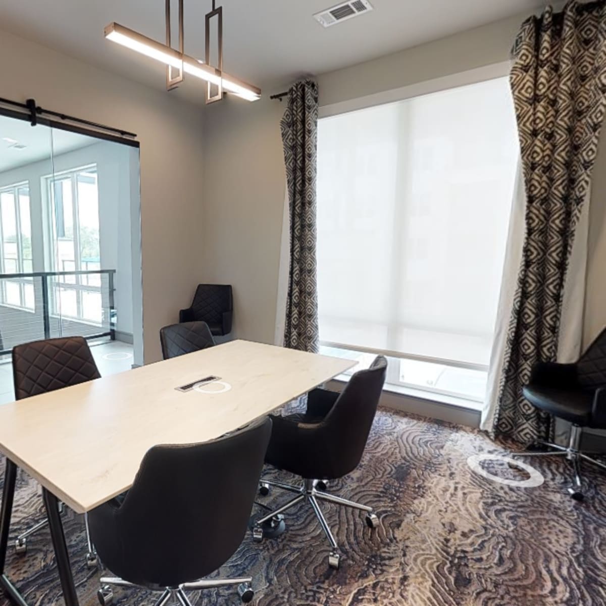 A modern conference room features a table surrounded by black chairs, with a glass partition leading to a bright, open space.
