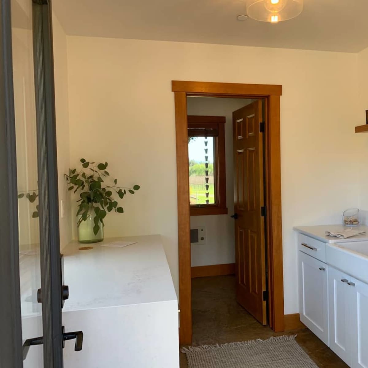 A modern bathroom with a white sink and cabinet, a door leading to another room, and a shelf with decorative items.