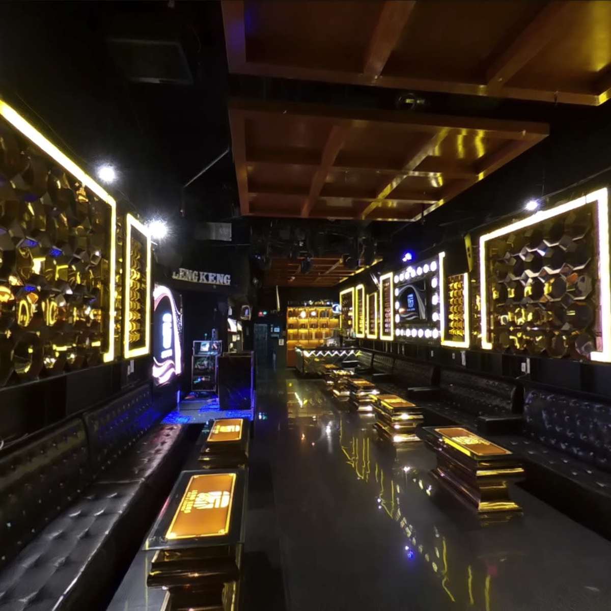 The interior of a dimly lit lounge features black leather seating, illuminated gold-framed wall designs, and sleek reflective surfaces.